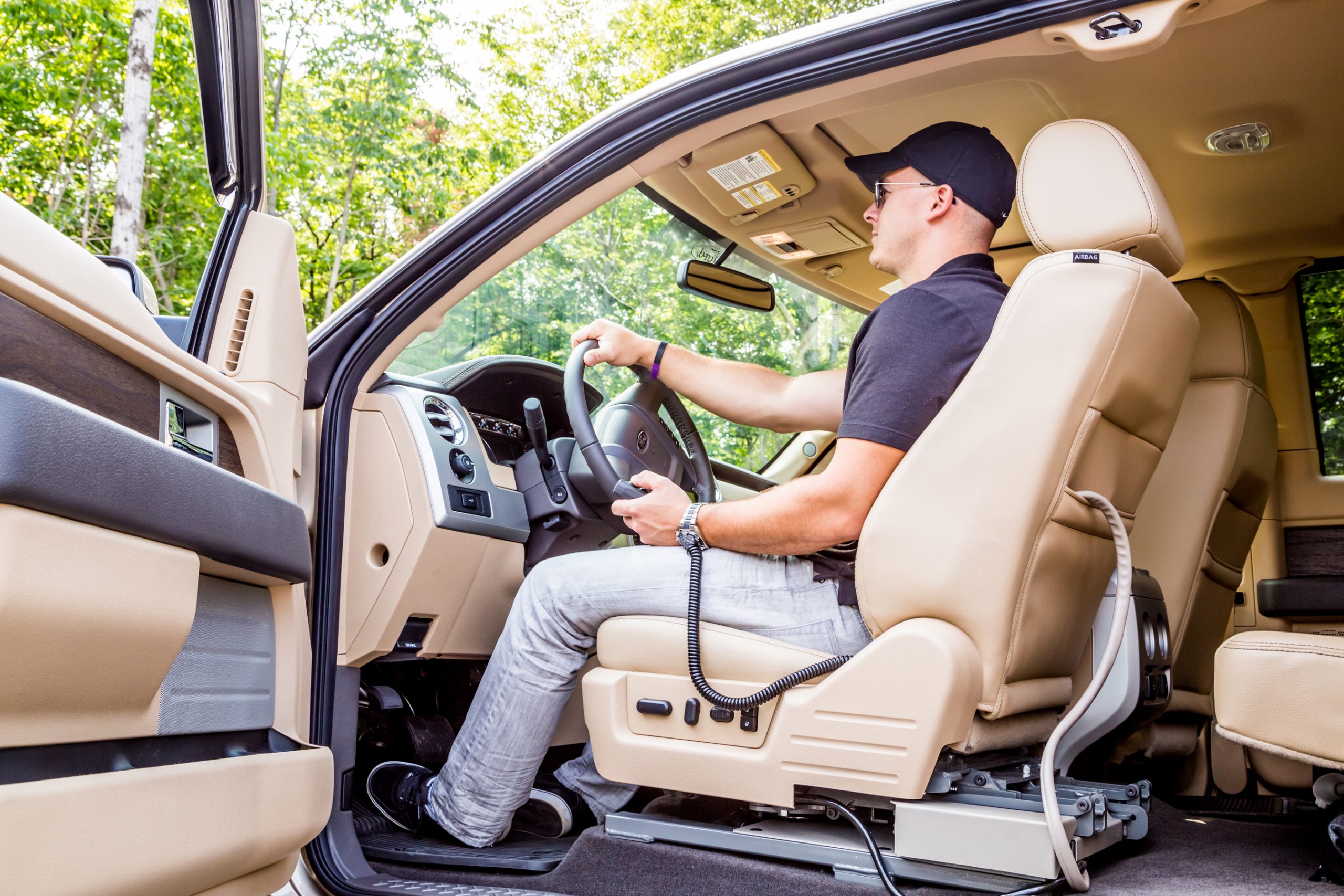 A man sits in the driver's seat of a Ford pickup truck holding the LINK pendant in his left hand and the steering wheel in his right hand (side angle)