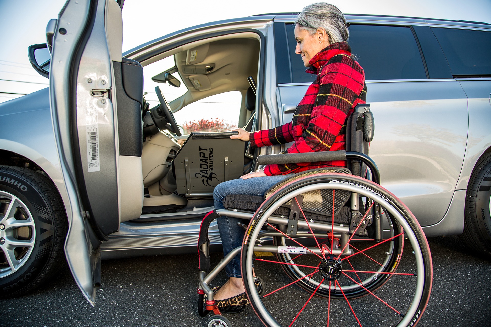 A woman flipping the transfer board of the ASENTO down while sitting in a ridgid frame manual wheelchair. (door fully open)